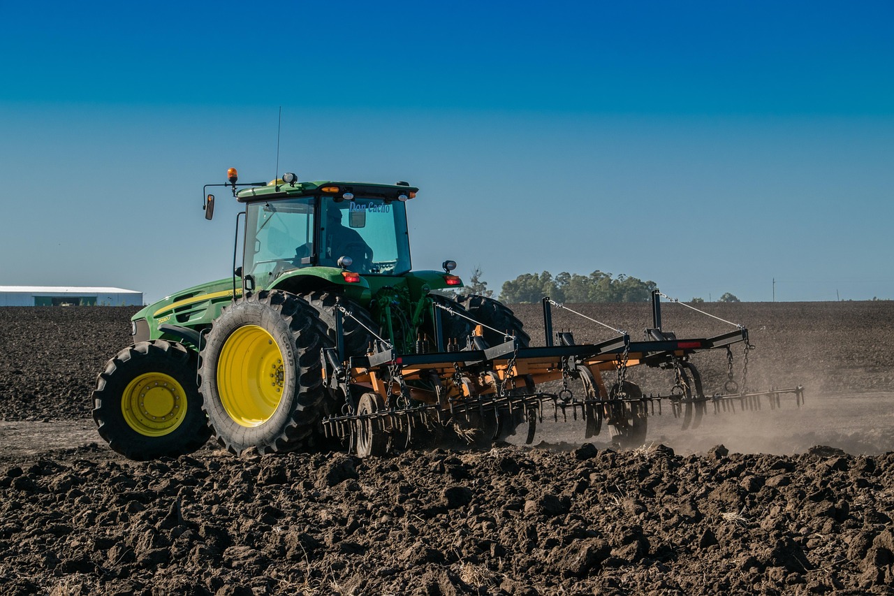 Tracteur vert labourant un champ agricole sous un ciel bleu.